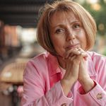 Charming senior woman with hands clasped enjoys a peaceful moment outside.