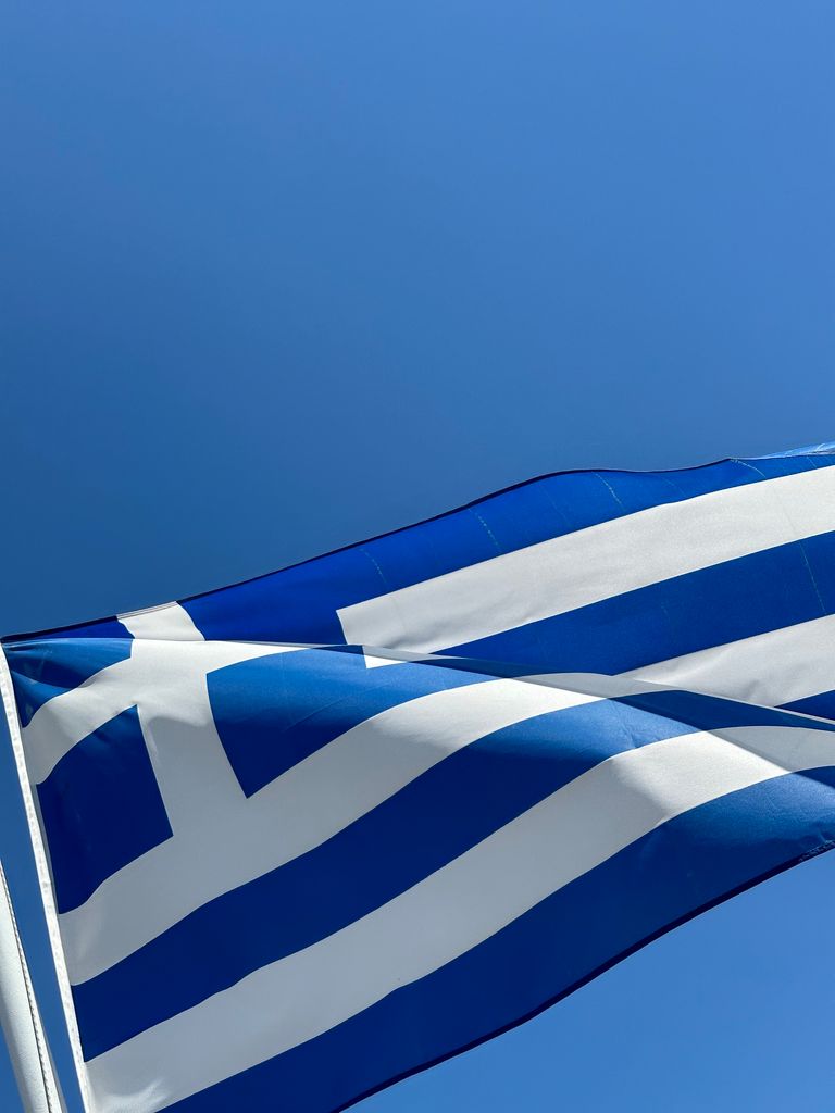 Close-up of the Greek national flag waving against a clear blue sky, capturing patriotism.
