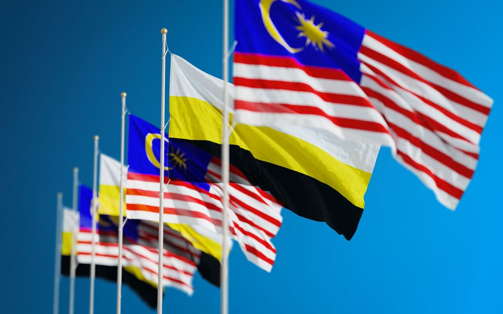 Close-up view of Malaysian and Perak state flags waving in the sky. Bold, patriotic colors stand out.